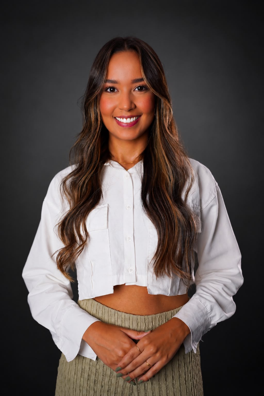 Retrato de Bruna sorrindo, com camisa branca e fundo escuro